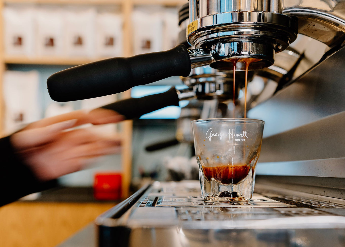 Espresso machine pouring coffee into a glass shot glass on a bar.