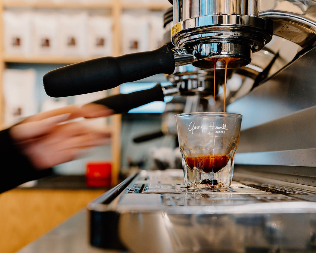 Espresso machine pouring coffee into a glass shot glass on a bar.